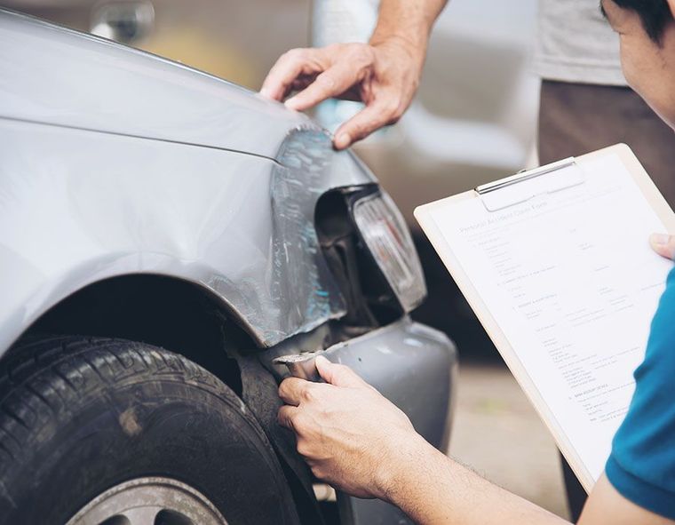 Mechanic inspecting a damaged gray car fender with a clipboard nearby