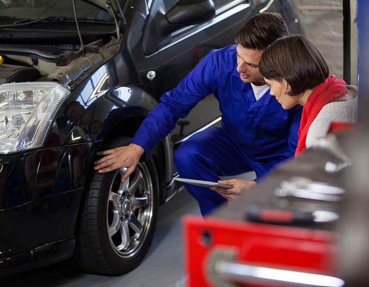 Mechanic in blue uniform inspecting a black car’s front wheel in a garage