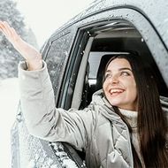 Smiling woman leaning out of a snowy car window and waving her hand