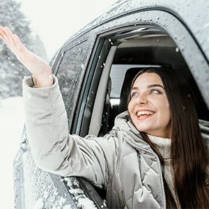 Smiling woman leaning out of a snowy car window and waving her hand