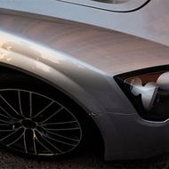 Close-up of a silver sports car’s front wheel and headlight on a dark road