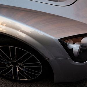 Close-up of a silver sports car’s front wheel and headlight on a dark road