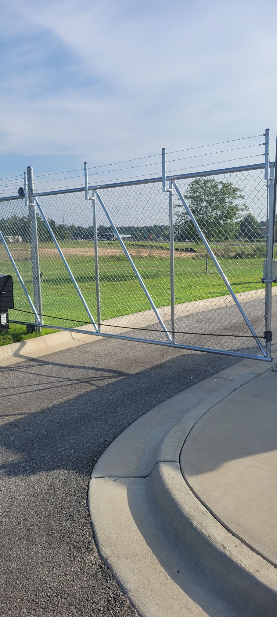 A chain link fence is sitting on the side of a road next to a concrete curb.