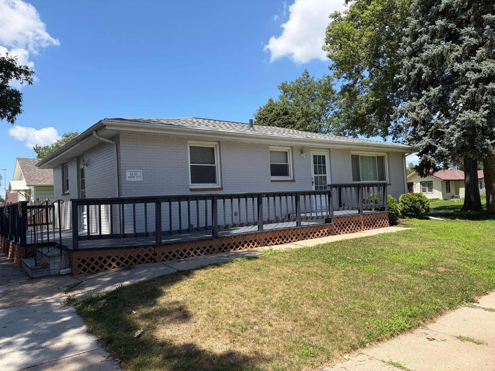 Single-story house with a front ramp, white siding, and a grassy yard under a blue sky