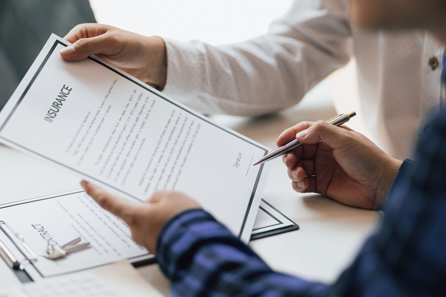Hands signing an insurance document on a desk, possibly a business setting. Hands signing an insurance document on a desk, possibly a business setting.