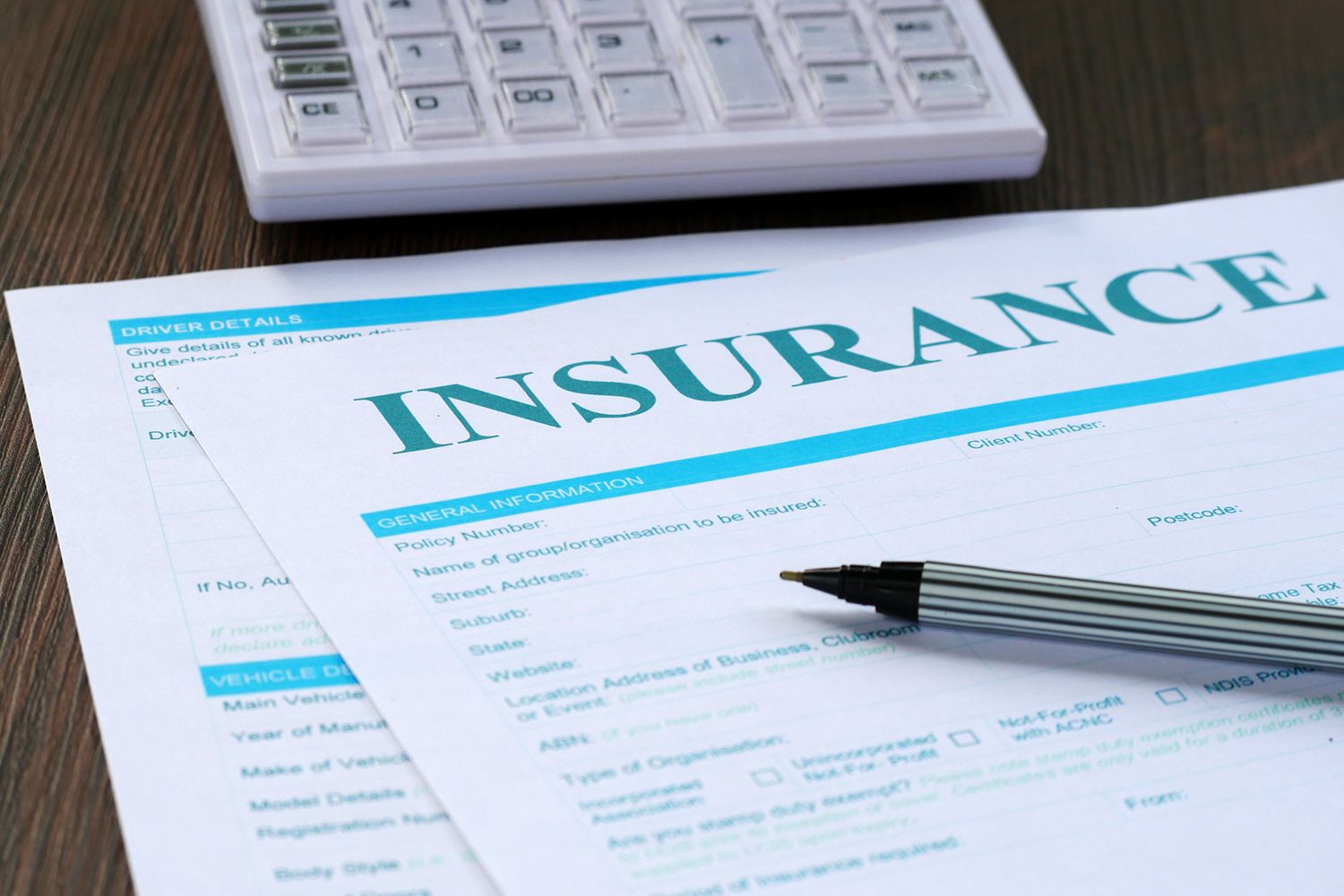 Insurance paperwork with a pen and calculator on a wooden table. Insurance paperwork with a pen and calculator on a wooden table.