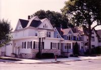 A street-level view of a white, multi-story Victorian-style building with a stone base and multiple gables.