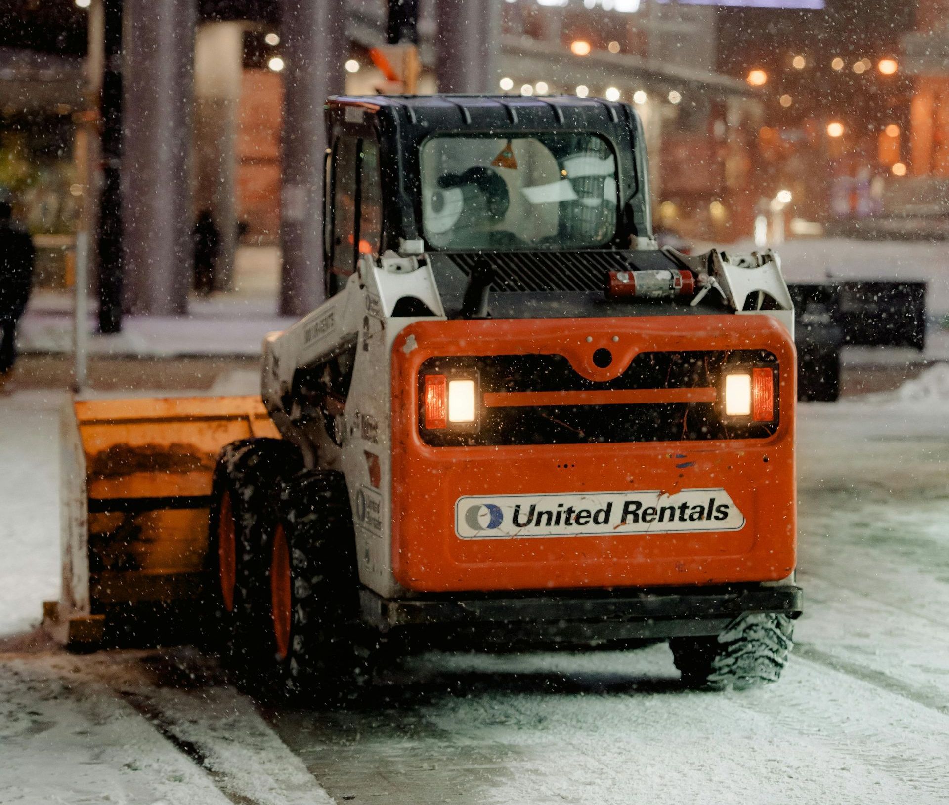 A united rentals snow plow is clearing snow from the street