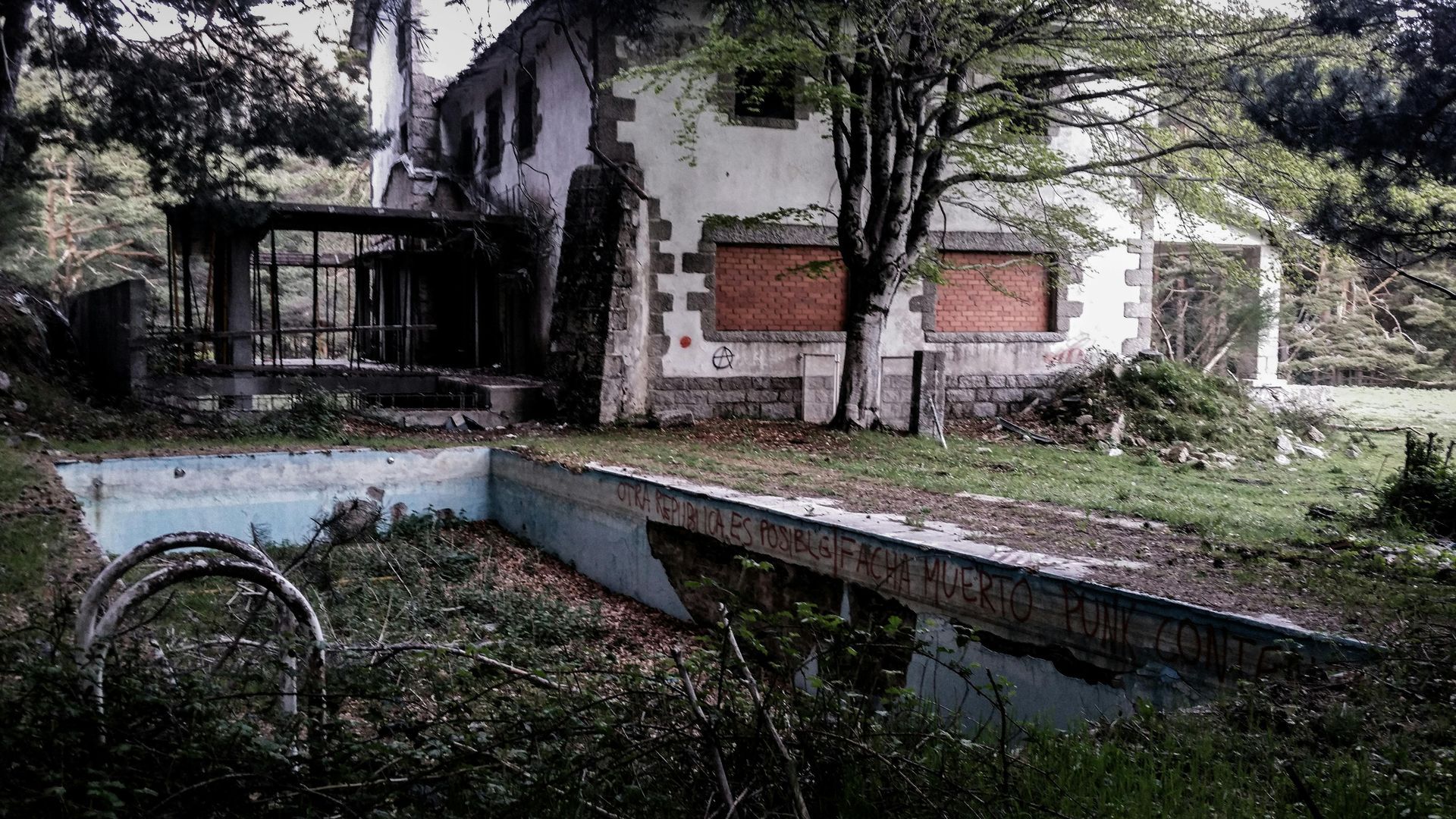 An old abandoned house with a swimming pool in front of it.