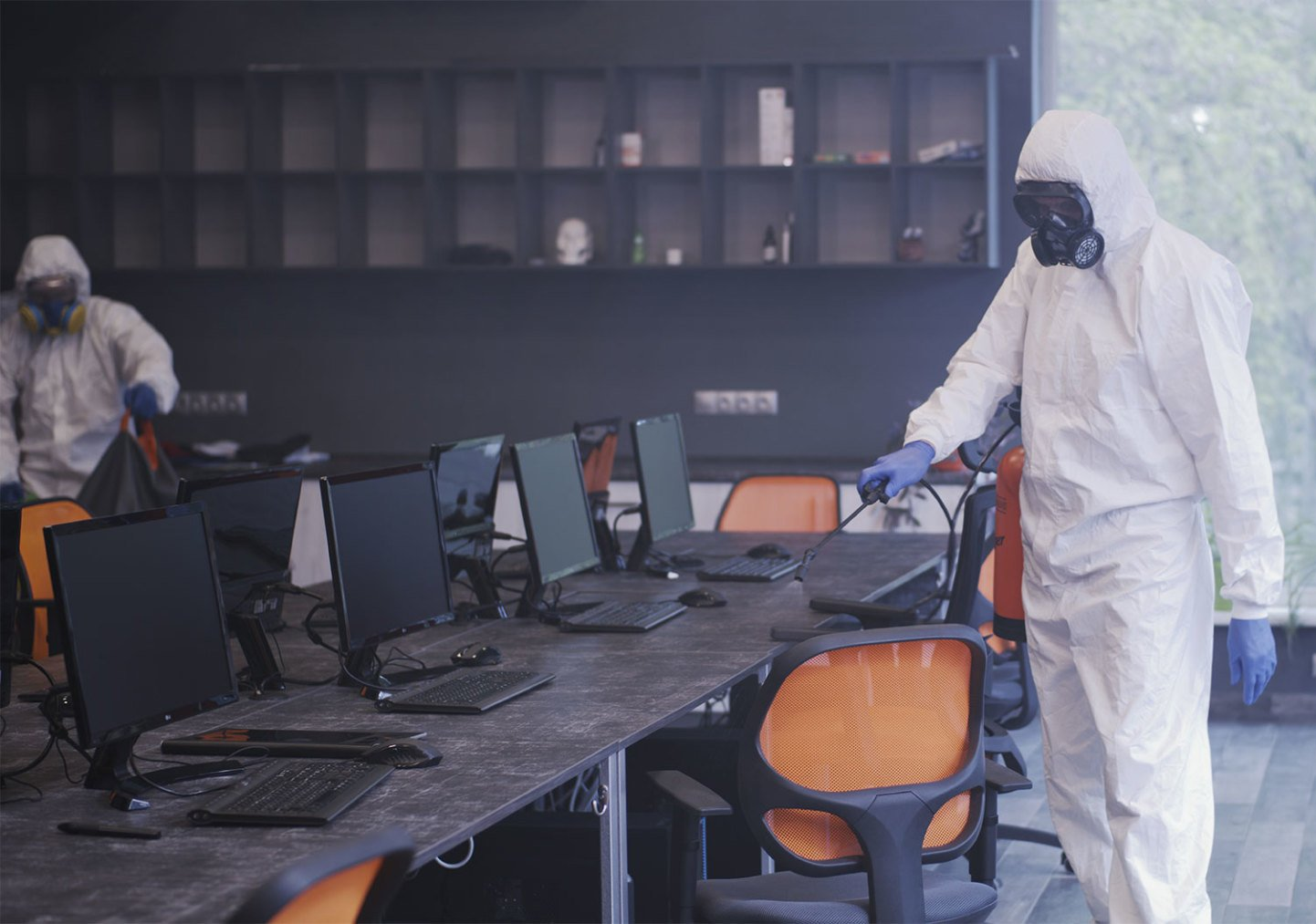 Office cleaners with blue aprons, yellow gloves cleaning office furniture, smiling.