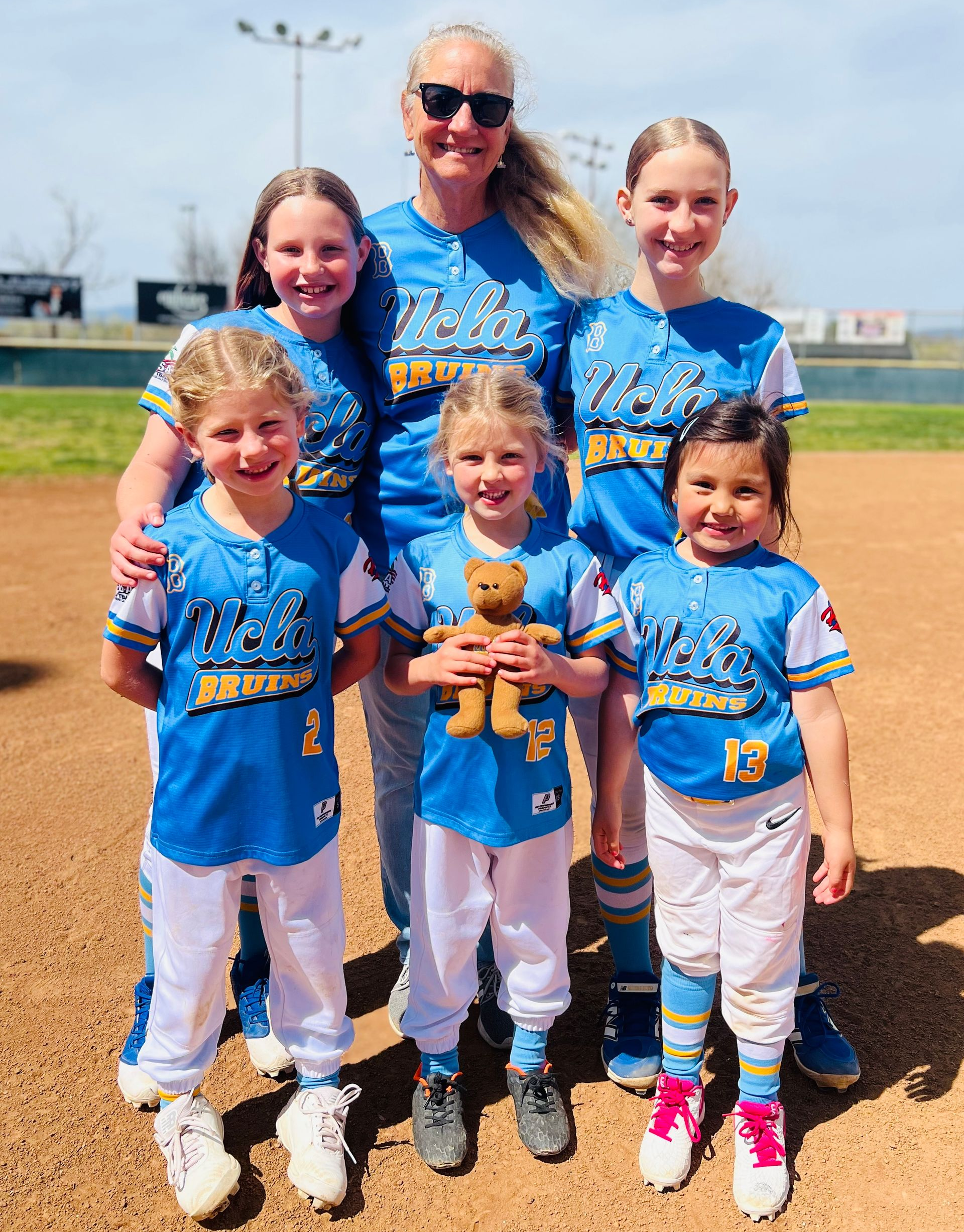 Man in green polo stands on a football field, arms crossed, stadium in background.