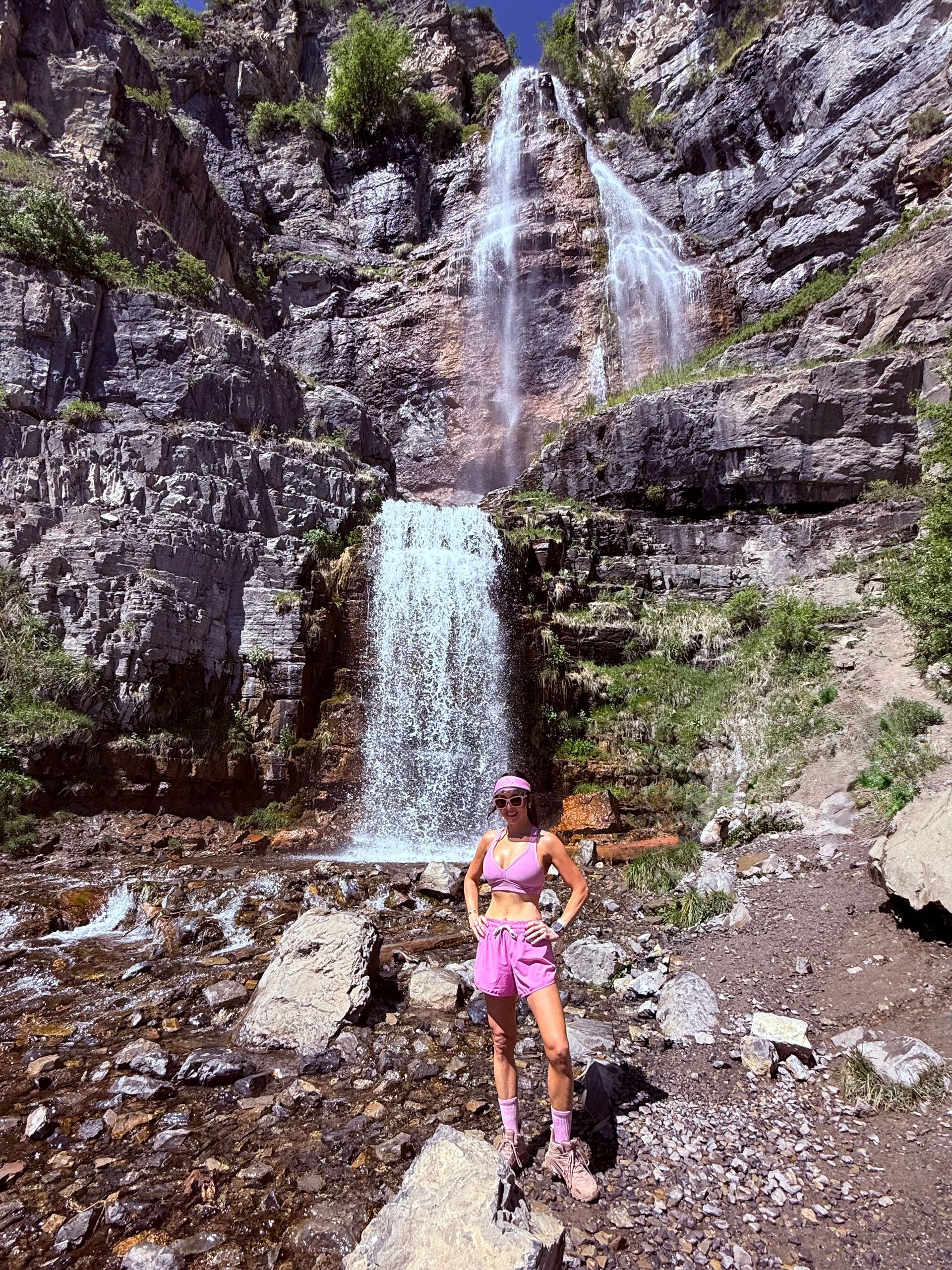 Person in pink stands before a waterfall cascading down a rocky cliff.