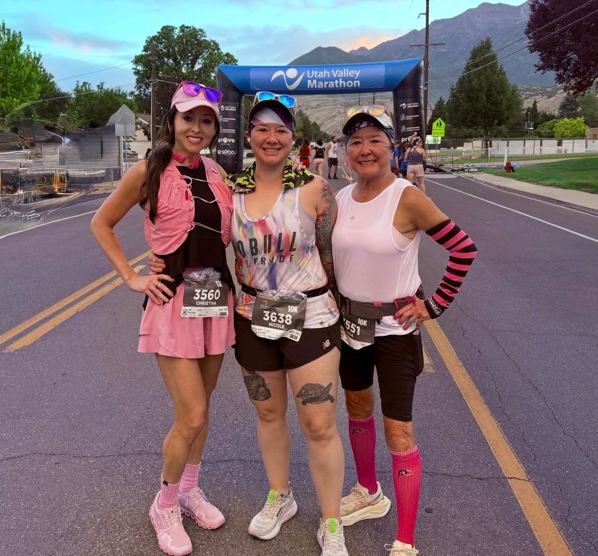 Three runners posing on a road at dawn with mountains and a race banner in the background.