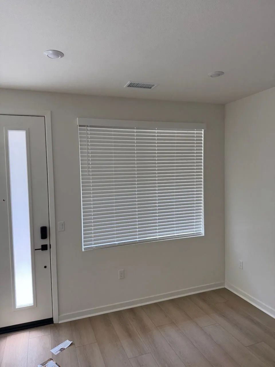 Empty room with white walls, wood-look floor, front door, and window blinds.