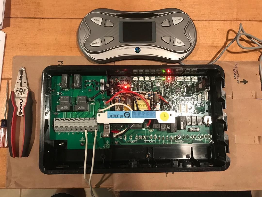 A remote control is sitting on a wooden table next to a pair of pliers.