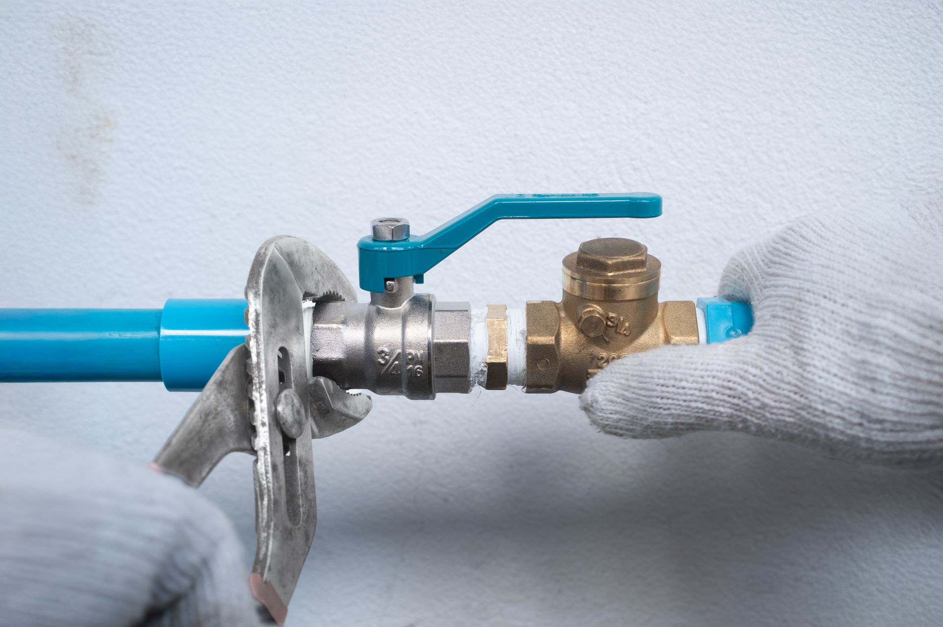 Gloved hands use a wrench to tighten a brass ball valve onto a blue PVC pipe. Gloved hands use a wrench to tighten a brass ball valve onto a blue PVC pipe.