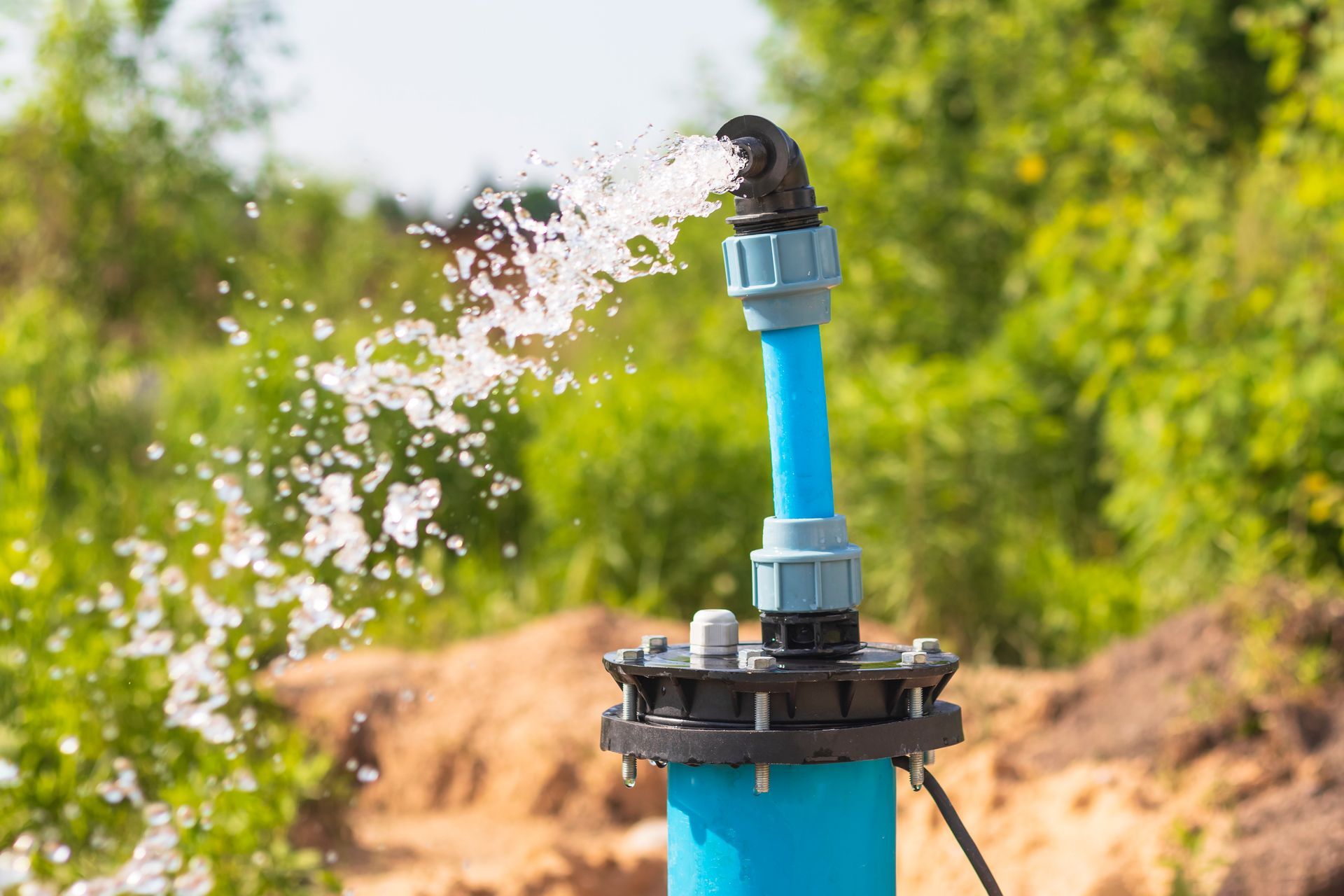 A blue water pump outlet sprays a steady stream of water into the air in a grassy outdoor setting. A blue water pump outlet sprays a steady stream of water into the air in a grassy outdoor setting.