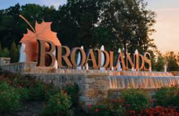 Broadlands entrance sign with stone wall, flowers, and trees at sunset Broadlands entrance sign with stone wall, flowers, and trees at sunset
