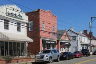 Small-town street with colorful storefronts, parked cars, and a clear blue sky Small-town street with colorful storefronts, parked cars, and a clear blue sky