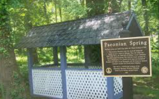 Wooden spring shelter in a wooded area with a sign reading “Paconian Spring” Wooden spring shelter in a wooded area with a sign reading “Paconian Spring”