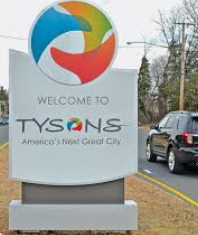 A Tysons, Virginia, welcome sign features a colorful abstract logo and the slogan America's Next Great City by a road.