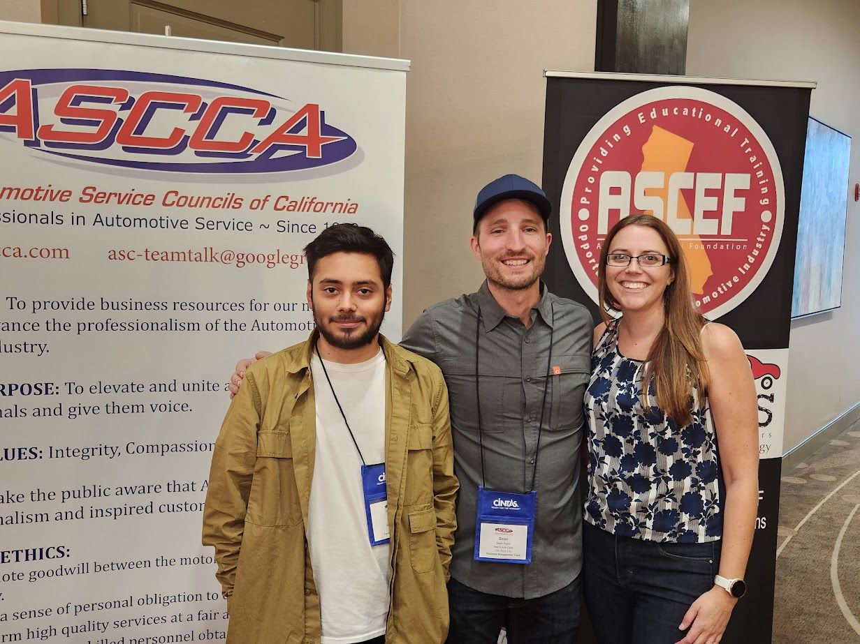 Three people are posing for a picture in front of a sign that says ascca