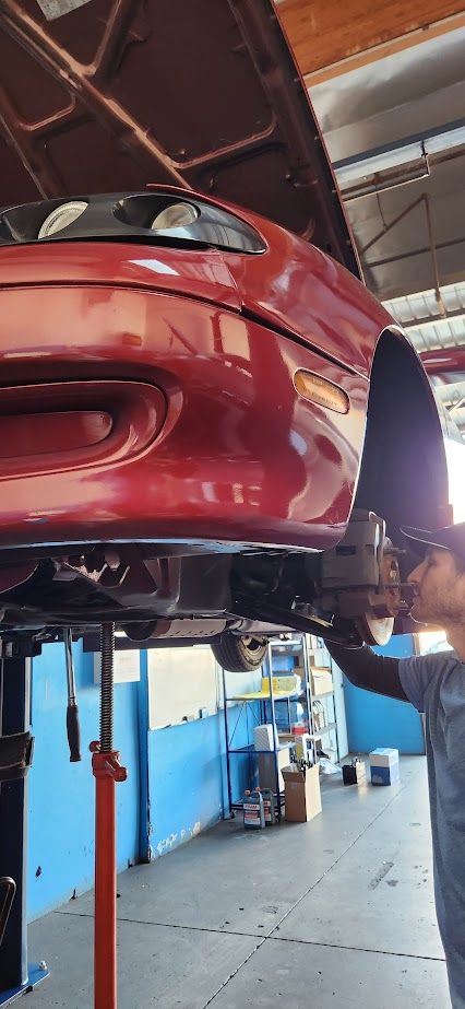 A man is working on a red car on a lift in a garage.