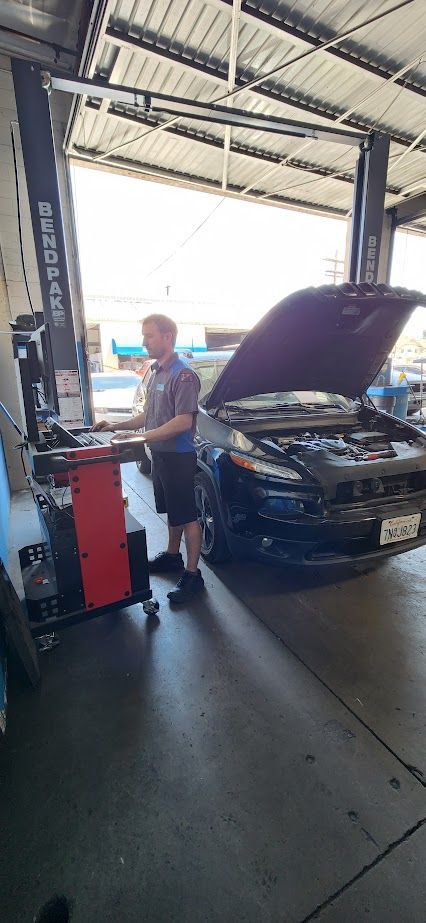 A man is working on a car in a garage with the hood up.