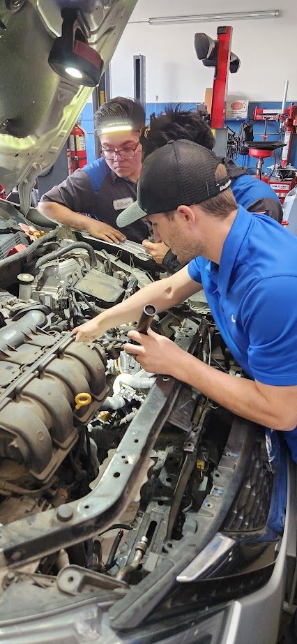 A group of mechanics are working on a car engine in a garage - Sean's Auto Care