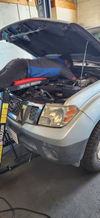 A man is working on the engine of a car with the hood open - Sean's Auto Care