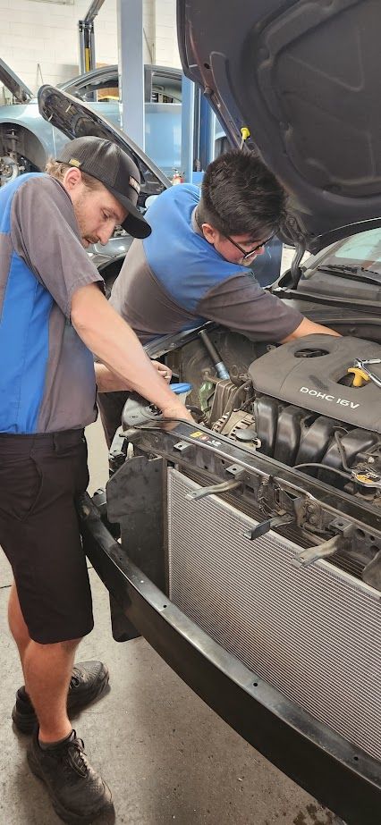 Two men are working on the engine of a car in a garage - Sean's Auto Care