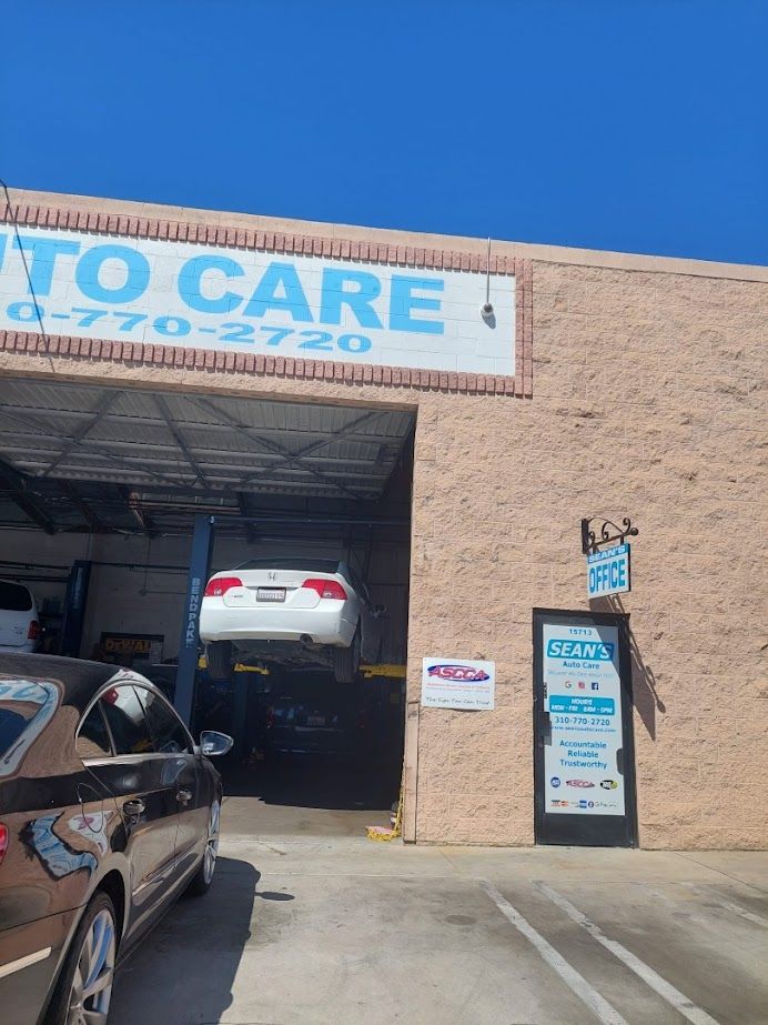 A car is on a lift in front of a building that says to care - Sean's Auto Care