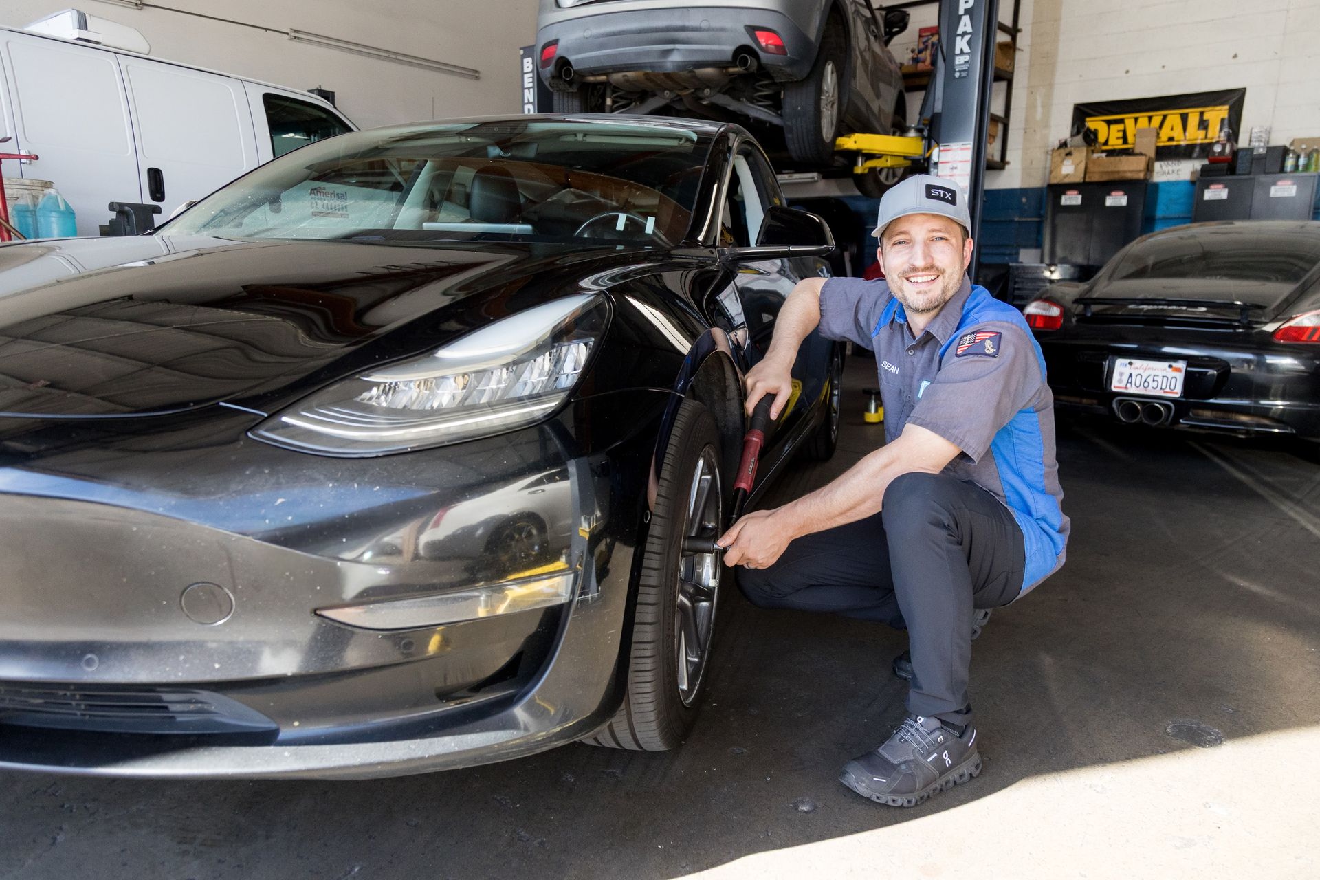 Man in a blue shirt crouches beside a black Tesla in an auto shop garage | Sean's Auto Care