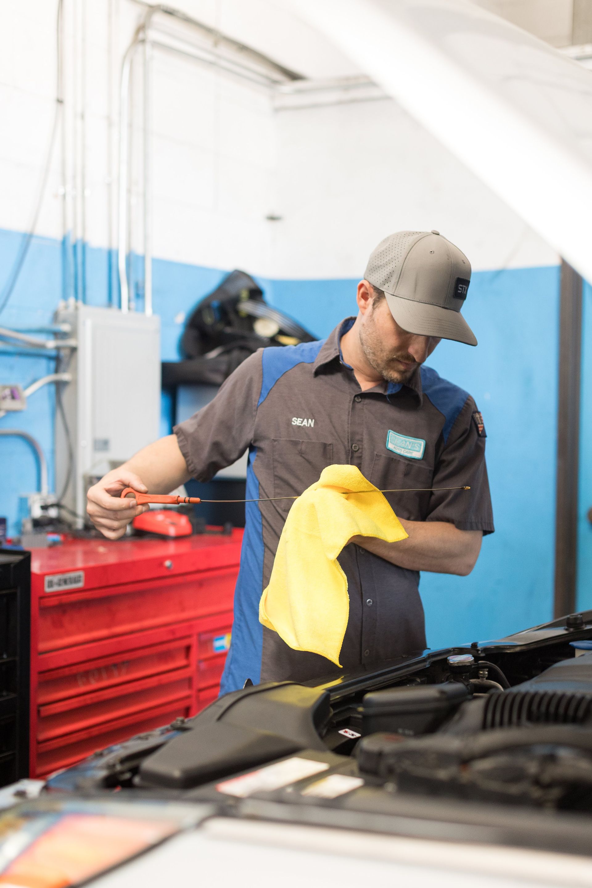 Mechanic in a garage wiping a car engine with a yellow cloth next to a red tool chest | Sean's Auto Care