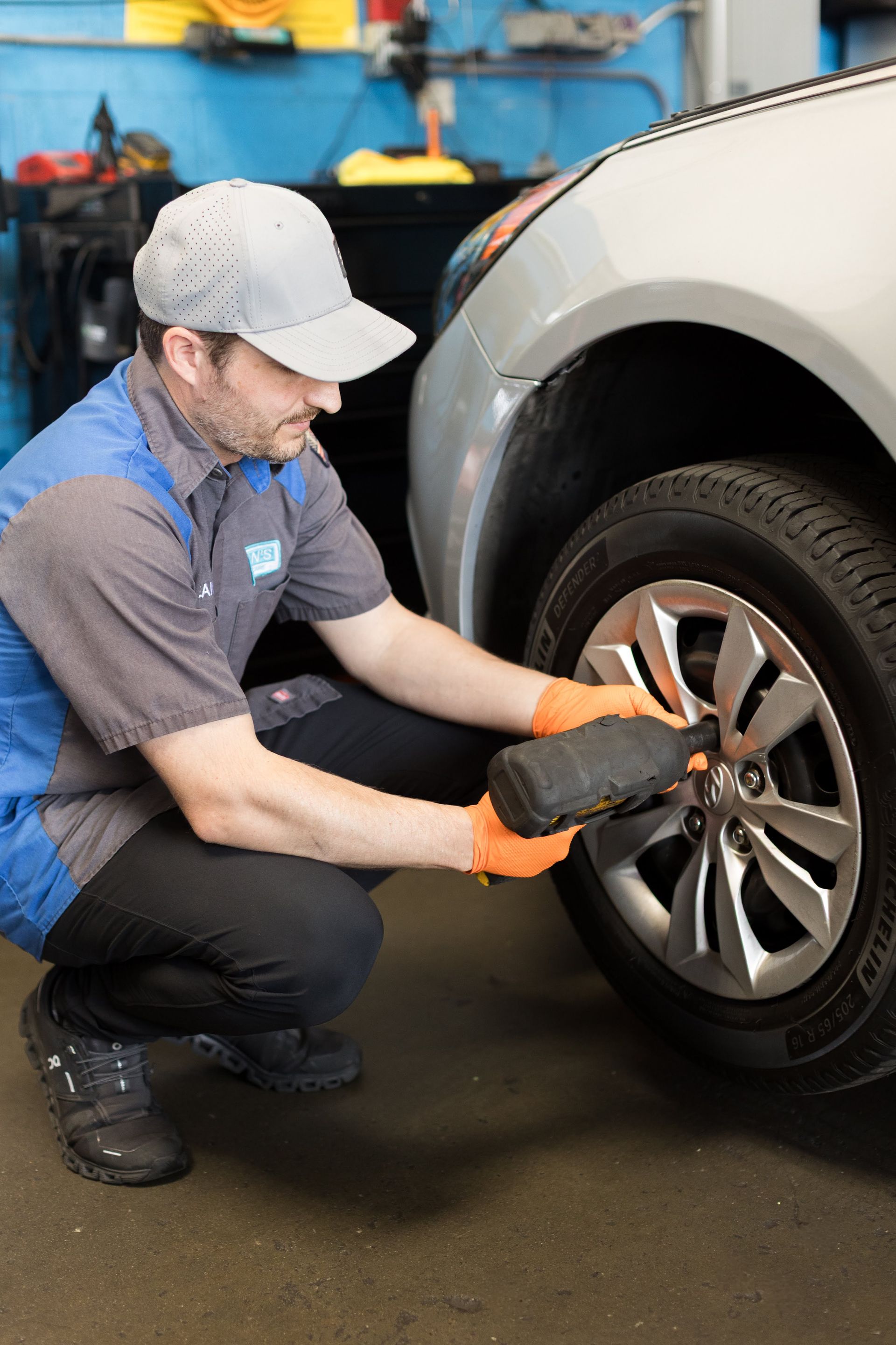 Mechanic tightening lug nuts on a car wheel in a garage, wearing orange gloves and a gray cap | Sean's Auto Care