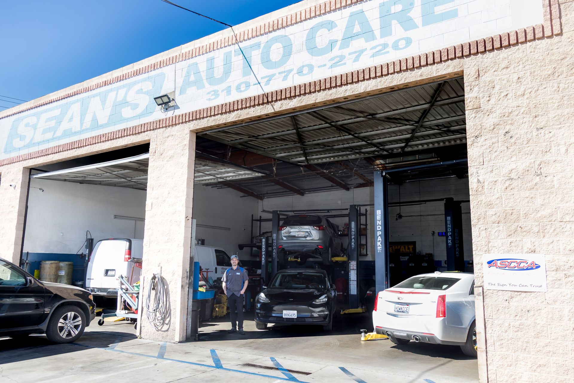 Auto repair shop exterior with open bays and several cars parked inside and outside | Sean's Auto Care