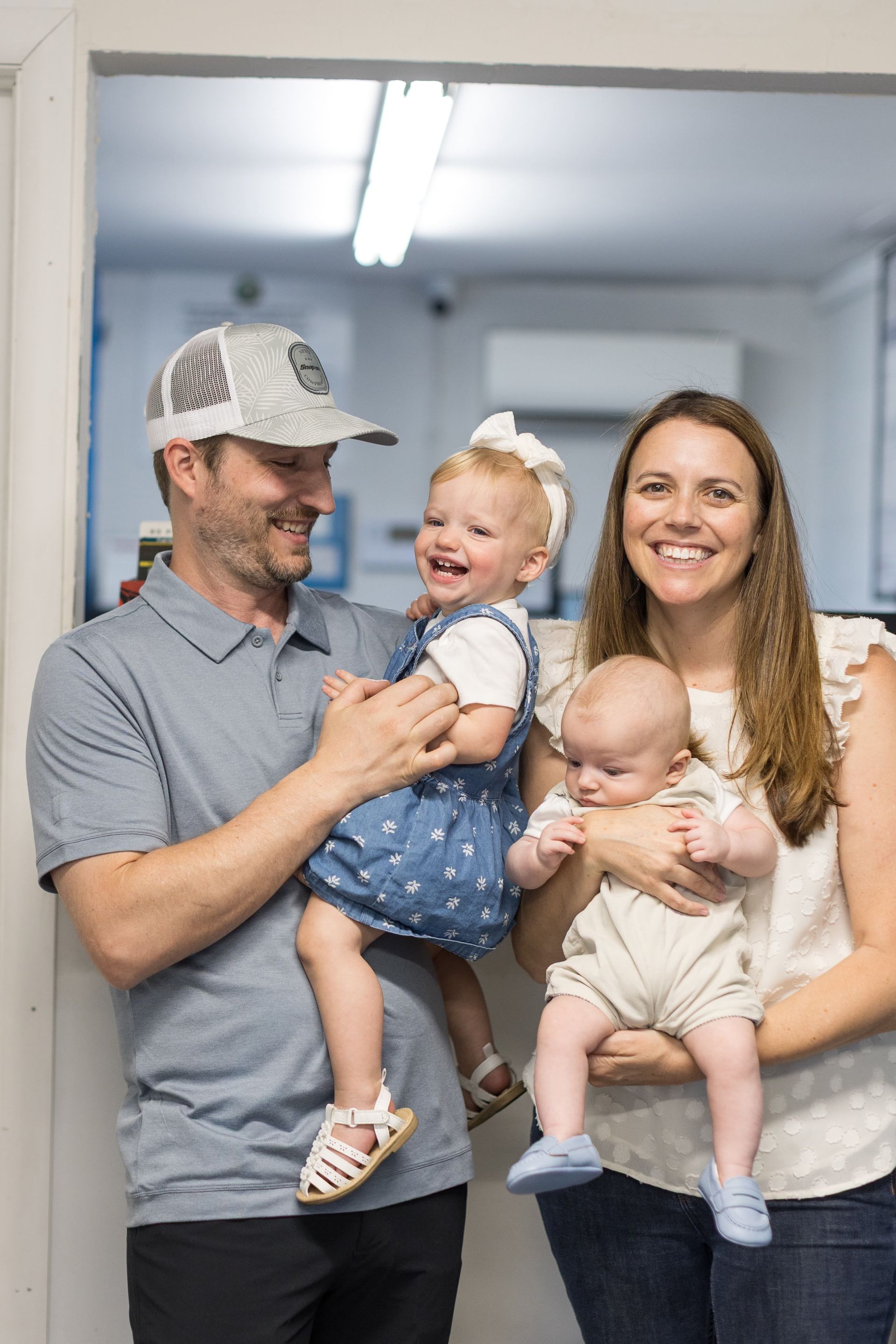 Family of four smiling indoors, with father holding a young child and mother holding a baby. | Sean's Auto Care