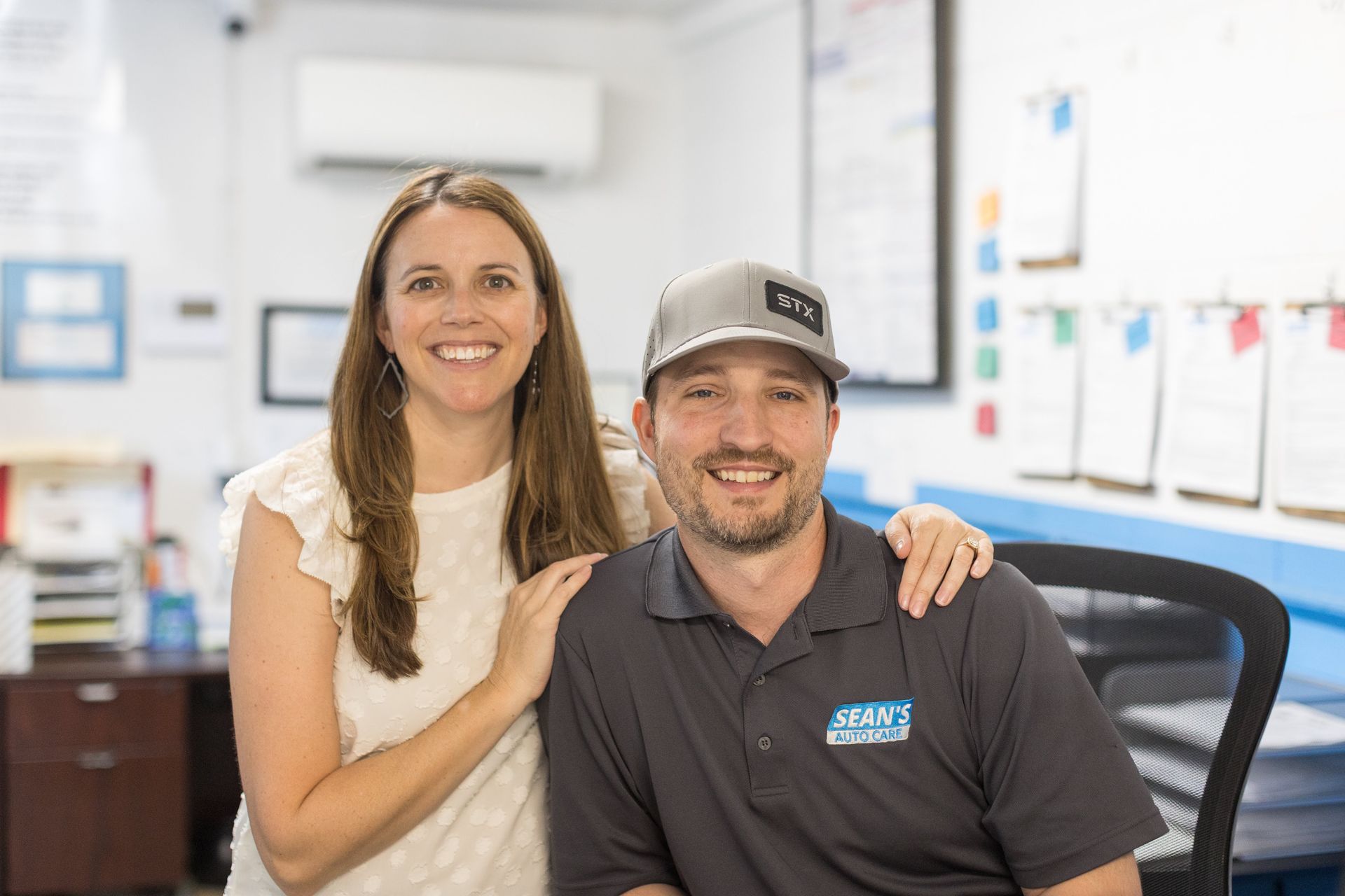 Two smiling coworkers in an office, seated together with one hand on the other's shoulder. | Sean's Auto Care