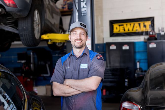 A man is standing next to a car engine in a garage - Sean's Auto Care
