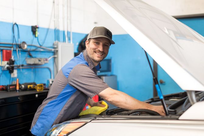 Three men are posing for a picture in front of a car in a garage - Sean's Auto Care