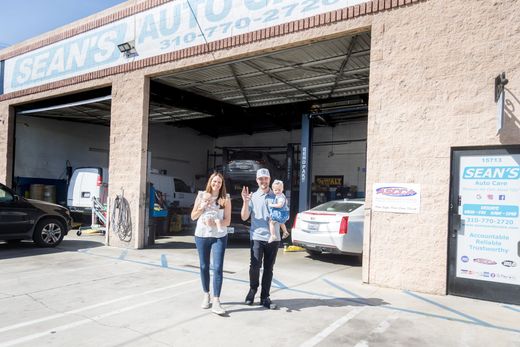 Two people standing outside an auto repair shop with open garage bays and cars inside. | Sean's Auto Care