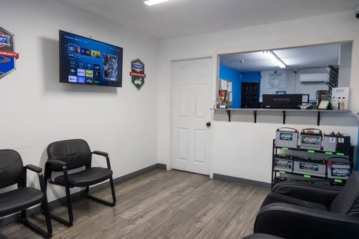 Office lounge with wall-mounted TV, black chairs, desk area, and wood-look flooring | Sean's Auto Care