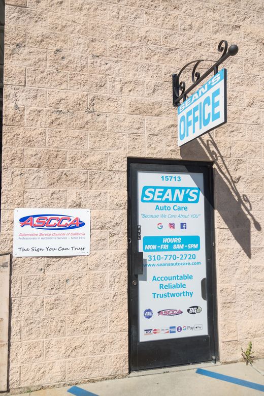 Storefront door with a blue “OFFICE” sign and “SEAN’S Auto C” lettering on a beige stucco wall | Sean's Auto Care