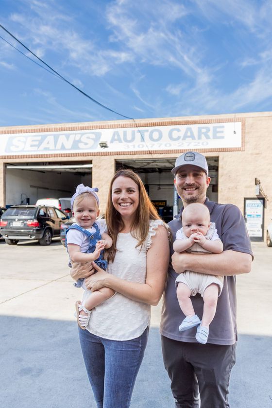 A man and a woman are standing in front of a sean auto shop - Sean's Auto Care