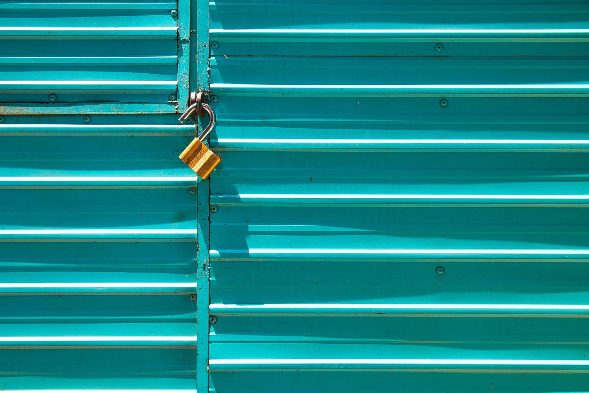 Teal corrugated metal gate secured by a yellow padlock.