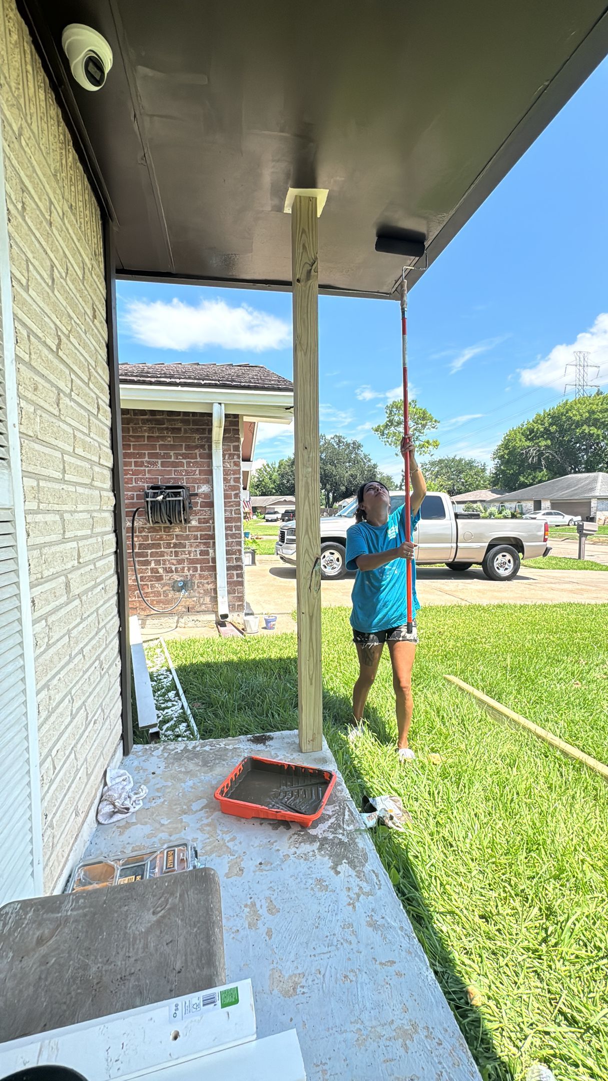 Person standing on a porch next to a porch post, with a grassy yard and parked pickup truck in the background