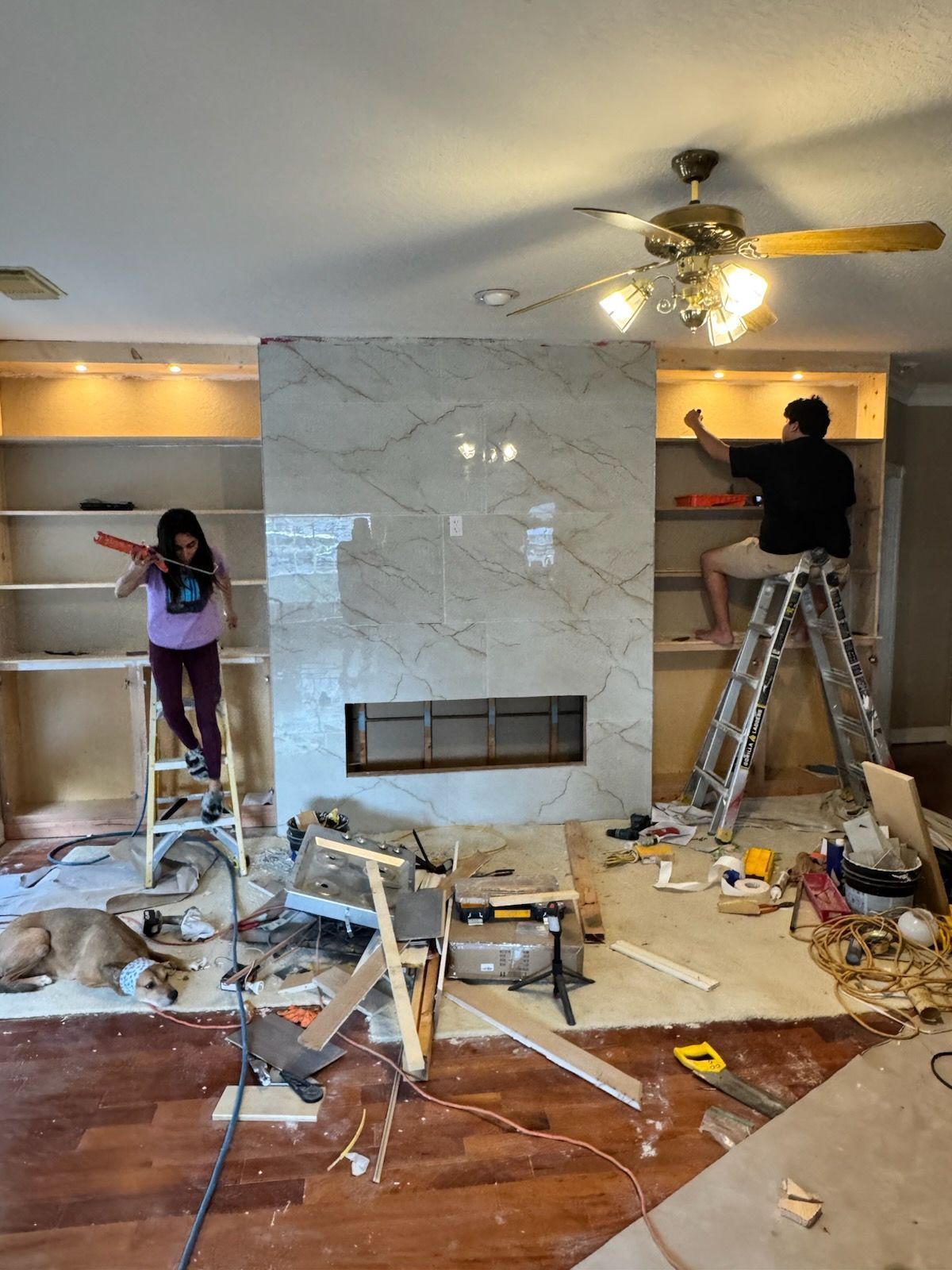 Two people working on a living room fireplace renovation amid tools and debris