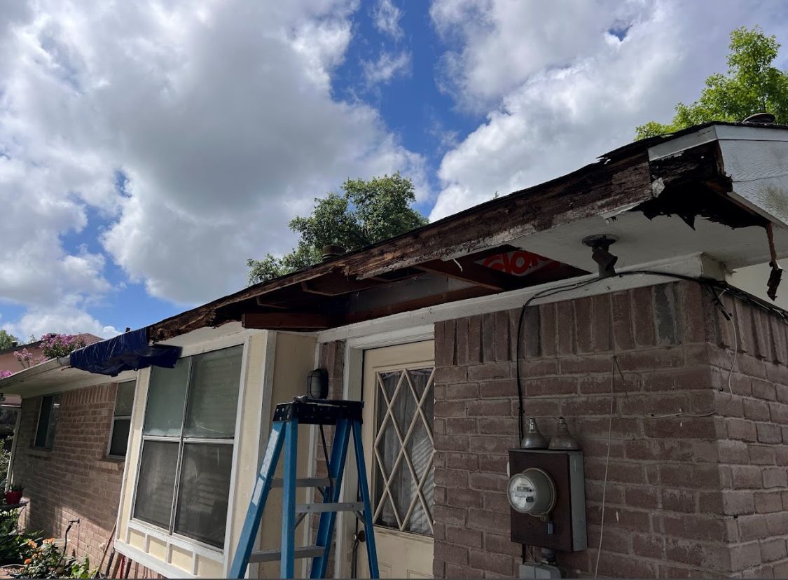 Damaged roof edge on a brick house with a blue ladder outside under a cloudy sky