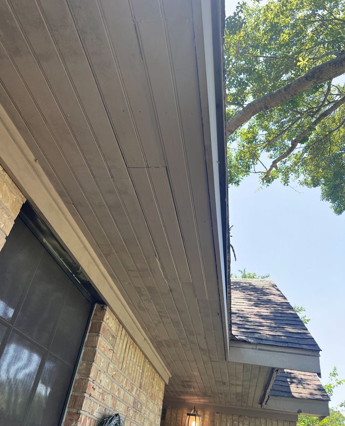 House eaves and tan brick wall viewed upward with trees and blue sky in the background