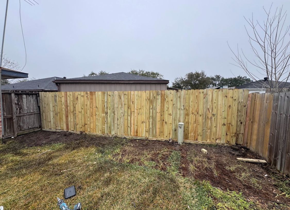 Backyard with a newly built wooden fence, patchy grass, and a gray overcast sky